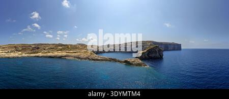 Ampia vista della baia di Dwejra su Gozo con scogliere calcaree, limpide acque del Mediterraneo e Fungus Rock sotto un cielo estivo blu. Foto Stock