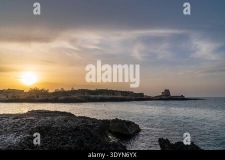 Vista mozzafiato del tramonto sulla costa di Roca Vecchia nel Salento. Il sole che tramonta illumina il mare Adriatico e il cielo, mettendo in risalto la torre medievale Foto Stock