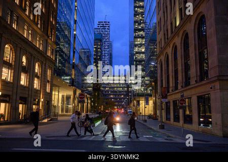 Toronto, ONTARIO, Canada - 11 novembre 2025: I pedoni attraversano la strada al crepuscolo nel centro di Toronto circondato da edifici illuminati. Foto Stock