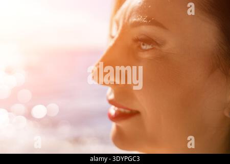 Profilo femminile al tramonto che guarda l'oceano durante l'ora d'oro con luce solare calda e sfondo bokeh Foto Stock