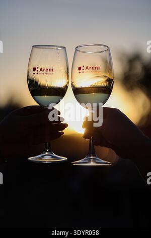 Due partecipanti brindano con bicchieri di vino bianco durante l'Areni Wine Festival al tramonto nel villaggio di Areni. Foto Stock