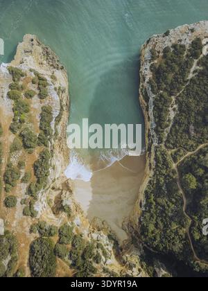 Vista aerea della spiaggia isolata annidata tra aspre scogliere, dove le acque turchesi si incontrano con la sabbia dorata in uno splendido abbraccio costiero, Porches, Faro Foto Stock