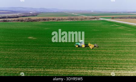 Vista aerea di un trattore che ara diligentemente campi verdi e si prepara per la stagione del raccolto, Novi Sad, Vojvodina, Serbia. Foto Stock