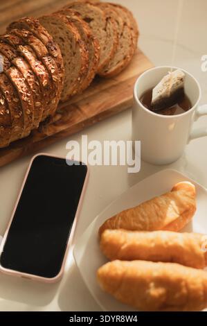 Colazione con pane, croissant, tè e smartphone Foto Stock