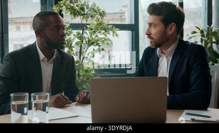 Due diversi uomini d'affari uomini multietnici team di lavoro in ufficio con laptop che parla di negoziazione manager uomo caucasico consulenza assicurativa africana Foto Stock