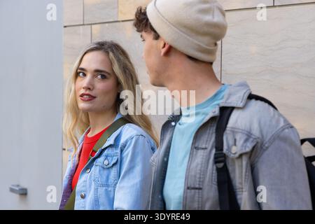 Coppia che cammina lungo un muro di pietra leggera, donna che si dirige verso l'uomo, indossa giacche di denim e zaino Foto Stock