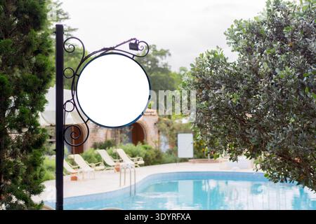 Mockup di cartellonistica bianca vuoto. Mock-up di un cartello circolare vuoto illuminato di fronte a una piscina. Spazio per testo, pubblicità all'aperto, banner. Foto Stock