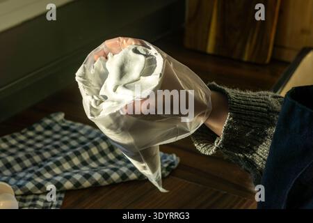 Primo piano di un sacchetto di pasticceria pieno di meringa lucida montata tenuta in mano. Foto Stock