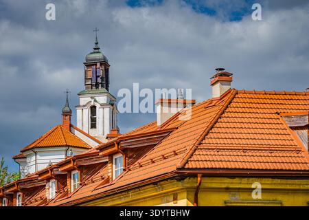 Primo piano dei tradizionali tetti di argilla arancione e di uno storico campanile bianco della chiesa sotto un suggestivo cielo nuvoloso a Vilnius, Lituania. Foto Stock