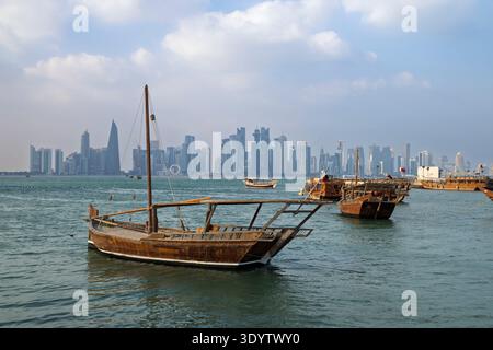 Tradizionali dhows arabi in legno lungo al Corniche con lo skyline della città alle spalle, Doha, Qatar Foto Stock