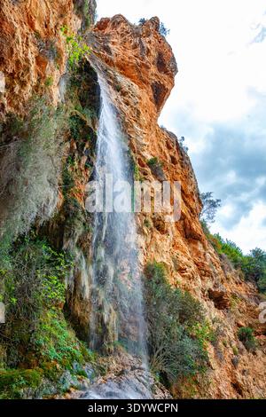 Una serena cascata sulle scogliere rocciose in una tranquilla piscina circondata da vegetazione lussureggiante Foto Stock