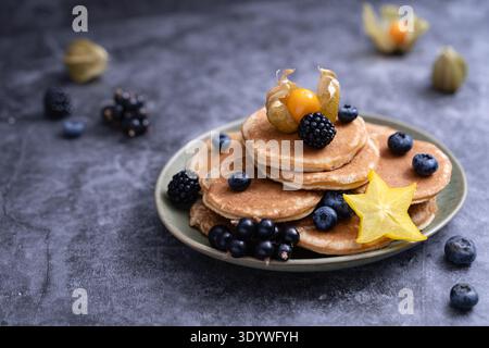 Una pila di pancake con mirtilli e contorno di frutta stellata su un piatto scuro con un'atmosfera soffusa Foto Stock