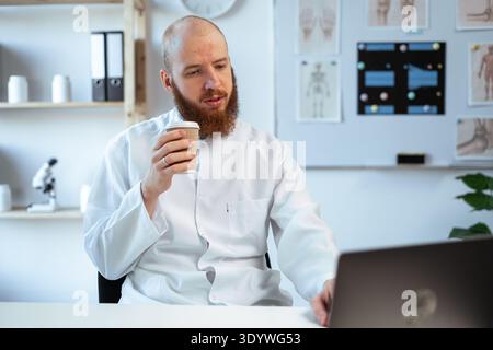 Medico maschile professionale che beve caffè controllo documenti medici sul posto di lavoro, analisi diagnosi paziente lavoro in ospedale. copia spazio Foto Stock