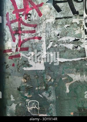Un'immagine astratta verticale e dettagliata di una parete urbana intemprata. La composizione presenta strati di carta spellabile, poster strappati, graffiti e creatina Foto Stock