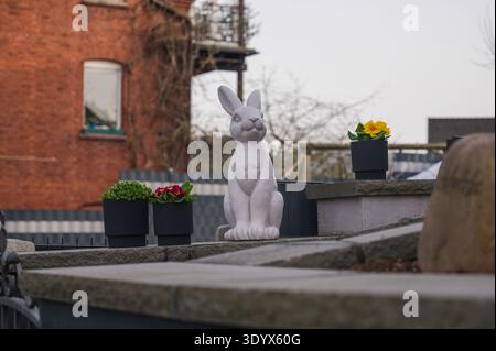 Statua bianca di coniglio in cemento si trova tra le piante in vaso su una sporgenza di pietra Foto Stock