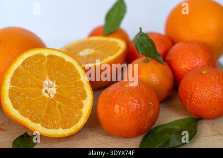 Agrumi freschi, compresi arancia a fette e mandarini interi con foglie verdi disposte su tagliere in legno. Cibo sano e naturale ricco di vita Foto Stock