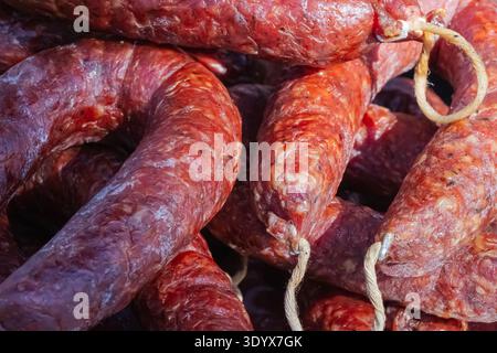 Primo piano dettagliato delle tradizionali salsicce stagionate legate con spago naturale e esposte in una bancarella del mercato locale, mettendo in risalto la consistenza rustica e l'artigianato Foto Stock