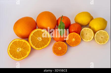 Assortimento di agrumi freschi, tra cui arance intere e affettate, mandarini e limoni disposti su sfondo chiaro. Cibo sano ricco di vitamina C.. Foto Stock