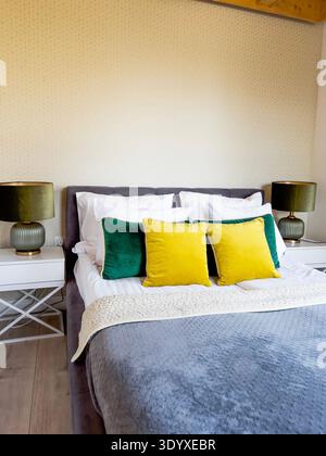 Camera moderna e accogliente con letto rivestito grigio e cuscini colorati in velluto Foto Stock