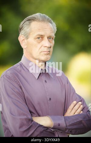Uomo più anziano in camicia viola che posa in parco per ritratti Foto Stock