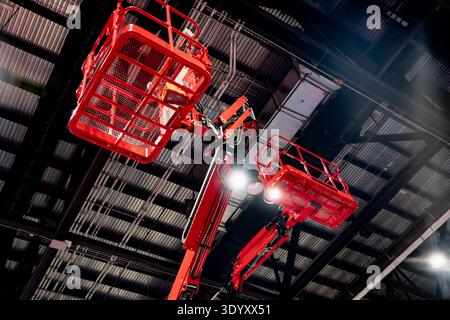 Esposizione interna di piattaforme aeree rosse con luci di lavoro luminose, noleggio di attrezzature abbinate, accesso al magazzino e temi tecnologici industriali Foto Stock