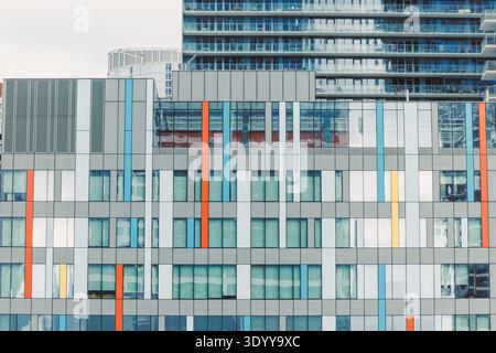 Una collezione di edifici moderni mostra diverse dimensioni e colori in una città trafficata. Le finestre in vetro riflettono il cielo sopra. Foto Stock