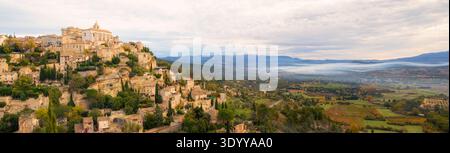 Gordes, Francia; villaggio collinare con fumo appeso nella valle sotto il punto panoramico Extrawide Foto Stock