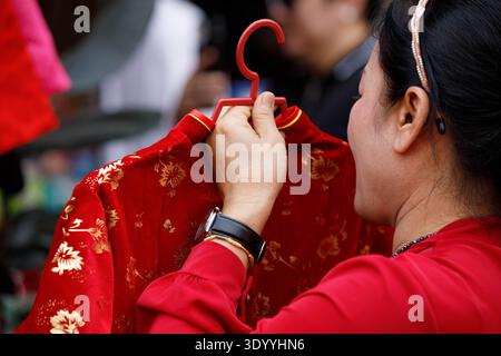Donna che sceglie vestiti, commerciante locale di strada, vita di strada tropicale, viaggiatore che esplora il mercato all'aperto, primo piano Foto Stock