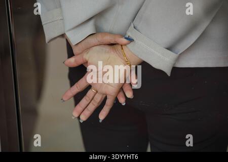 Le mani della donna incrociate dietro la schiena mentre si appoggiano contro la parete di vetro, movimento senza posa, movimento naturale e schietto, primo piano. Foto Stock