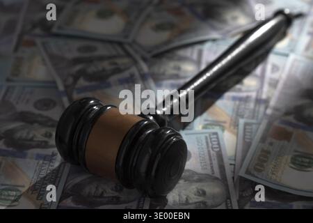 Martelletto nero su un mucchio di banconote da cento dollari. Concetto di corruzione aziendale, corruzione, criminalità da colletti bianchi e costi finanziari del sistema legale. Foto Stock