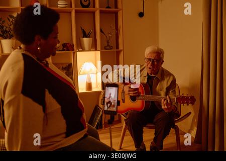 Uomo caucasico senior che suona la chitarra per la donna nera di mezza età a casa Foto Stock