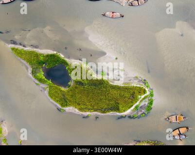 Vista aerea di una vivace isola verde abbracciata dalle rive sabbiose del fiume e dalle barche tradizionali, una tranquilla scena artistica della natura, Tetulia, Rangpur Foto Stock