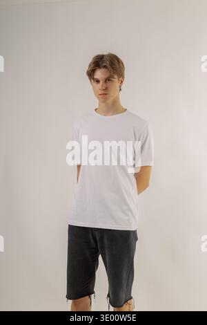 Bel giovane ragazzo in abiti eleganti su sfondo bianco in uno studio fotografico che posa per la fotocamera Foto Stock