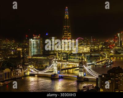 Vista aerea del Tower Bridge e dello Shard scintillano di luce dorata contro le acque scure del Tamigi, Londra, Greater London, Regno Unito. Foto Stock