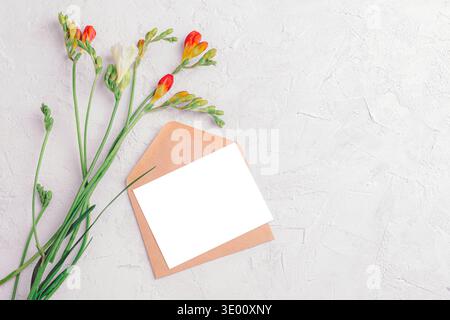 Fiori freesia con busta e biglietto d'auguri bianco su sfondo a trama leggera. Vista dall'alto, posizione piatta, mockup. Foto Stock