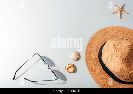 Accessori da spiaggia estivi con cappello di paglia, occhiali da sole e conchiglie su sfondo blu che simboleggiano il relax e la vacanza. Vista dall'alto, letto piatto, fotocopiatrice Foto Stock