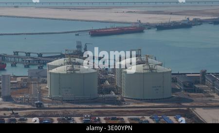 Vista aerea di enormi serbatoi industriali bianchi che brillano sotto il sole accanto a un porto con navi, Mappa Ta Phut, Rayong, Thailandia. Foto Stock