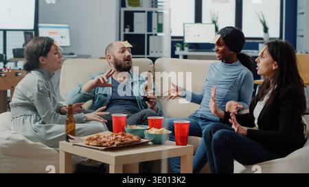 Gruppo multietnico di colleghi che si divertono a indovinare giochi e bevande. Compagni di lavoro che giocano a sciarade e usano note adesive sulla fronte per festeggiare la festa con l'intrattenimento dopo il lavoro Foto Stock