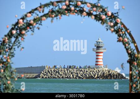 Un faro a righe rosse e bianche si erge alto lungo il mare Foto Stock