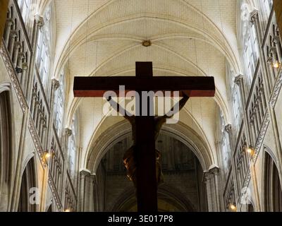 Una silhouette di un crocifisso in legno si erge contro l'alto soffitto a volta gotico e gli archi a costine della Cattedrale di Rouen, immersi in morbidi ed eterei Foto Stock