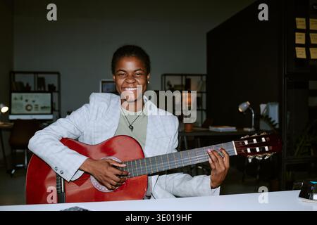 Ritratto della giovane donna nera adulta sorridente mentre suona la chitarra acustica Foto Stock