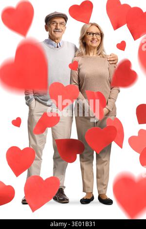 Coppia matura che posa in abbraccio sotto la pioggia di cuori isolati su sfondo bianco Foto Stock