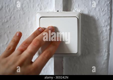 ILLUSTRAZIONE - 05 marzo 2026, Internazionale, Berlino: Una donna aziona un interruttore della luce su una parete. L'aumento dei costi dell'elettricità e dell'energia è un onere per molte famiglie e viene spesso discusso in relazione all'inflazione e al costo della vita più elevato. Foto: ELISA Schu/dpa Foto Stock