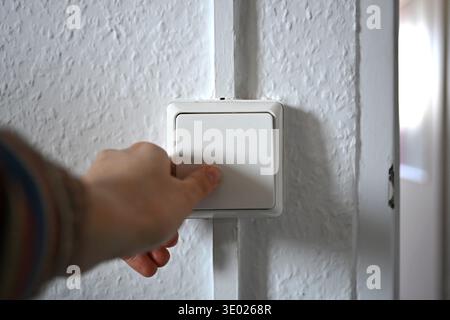 ILLUSTRAZIONE - 05 marzo 2026, Internazionale, Berlino: Una donna aziona un interruttore della luce su una parete. L'aumento dei costi dell'elettricità e dell'energia è un onere per molte famiglie e viene spesso discusso in relazione all'inflazione e al costo della vita più elevato. Foto: ELISA Schu/dpa Foto Stock