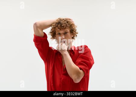 Un giovane uomo elegante con i capelli ricci sta posando in uno studio, indossando una camicia rossa vibrante. Foto Stock
