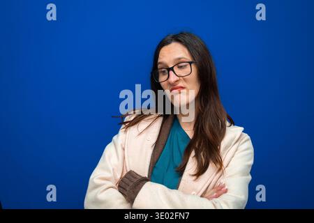 Donna che indossa occhiali sgombrati e che mostra dispiacere o disaccordo, in piedi con le braccia incrociate su sfondo blu Foto Stock