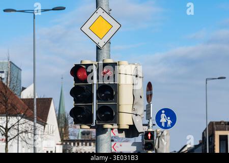 I semafori mostrano segnali rossi per auto e biciclette in una zona trafficata della città. Nelle vicinanze è presente un cartello pedonale che indica un passaggio sicuro. Il cielo è il massimo Foto Stock