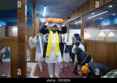 Un devoto adoratore Sikh porta il loro libro sacro sulla testa per essere messo a dormire in un letto del tempio. Nelle regine, a New York. Foto Stock