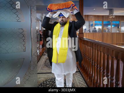 Un devoto adoratore Sikh porta il loro libro sacro sulla testa per essere messo a dormire in un letto del tempio. Nel Queens, New York. Foto Stock