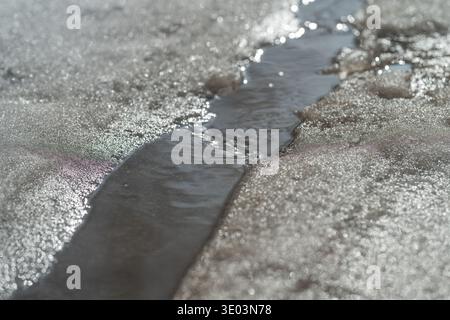 Tortuoso corso d'acqua attraverso la neve. Acqua fluente che taglia attraverso paesaggi innevati. Percorso serpeggiante dell'acqua di fusione che attraversa neve e ghiaccio durante l'inverno Foto Stock